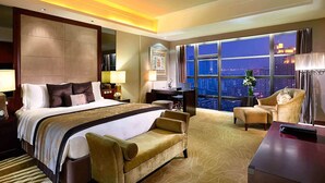 Une chambre d’hôtel avec un grand lit, un bureau, une chaise et une vue sur la ville la nuit.
