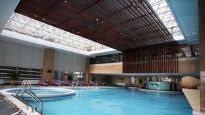 Une piscine intérieure dotée d’un bar, de chaises longues et d’un haut plafond agrémenté d’une verrière.