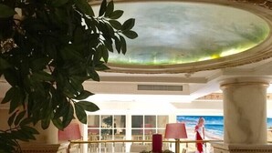 A dining area with a view of the ocean, featuring a round table and chairs, a red candle centerpiece, and a large column. - Hotel Gelibolu (Gallipoli)