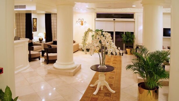 A spacious lobby with a high ceiling, a central floral arrangement, and a seating area with sofas and a coffee table. - Hotel Gelibolu (Gallipoli)