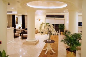 Um hall amplo com teto alto, um arranjo floral central e uma área de estar com sofás e uma mesa de centro.