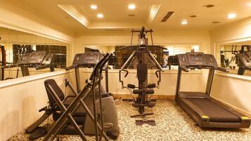 A gym with treadmills, an elliptical, and a stationary bike, featuring a mirrored wall and carpeted floor.