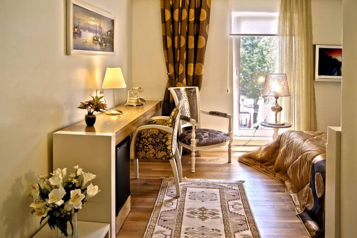 Un salon confortable avec un canapé, un fauteuil, un bureau avec une lampe et une vue sur l’extérieur.