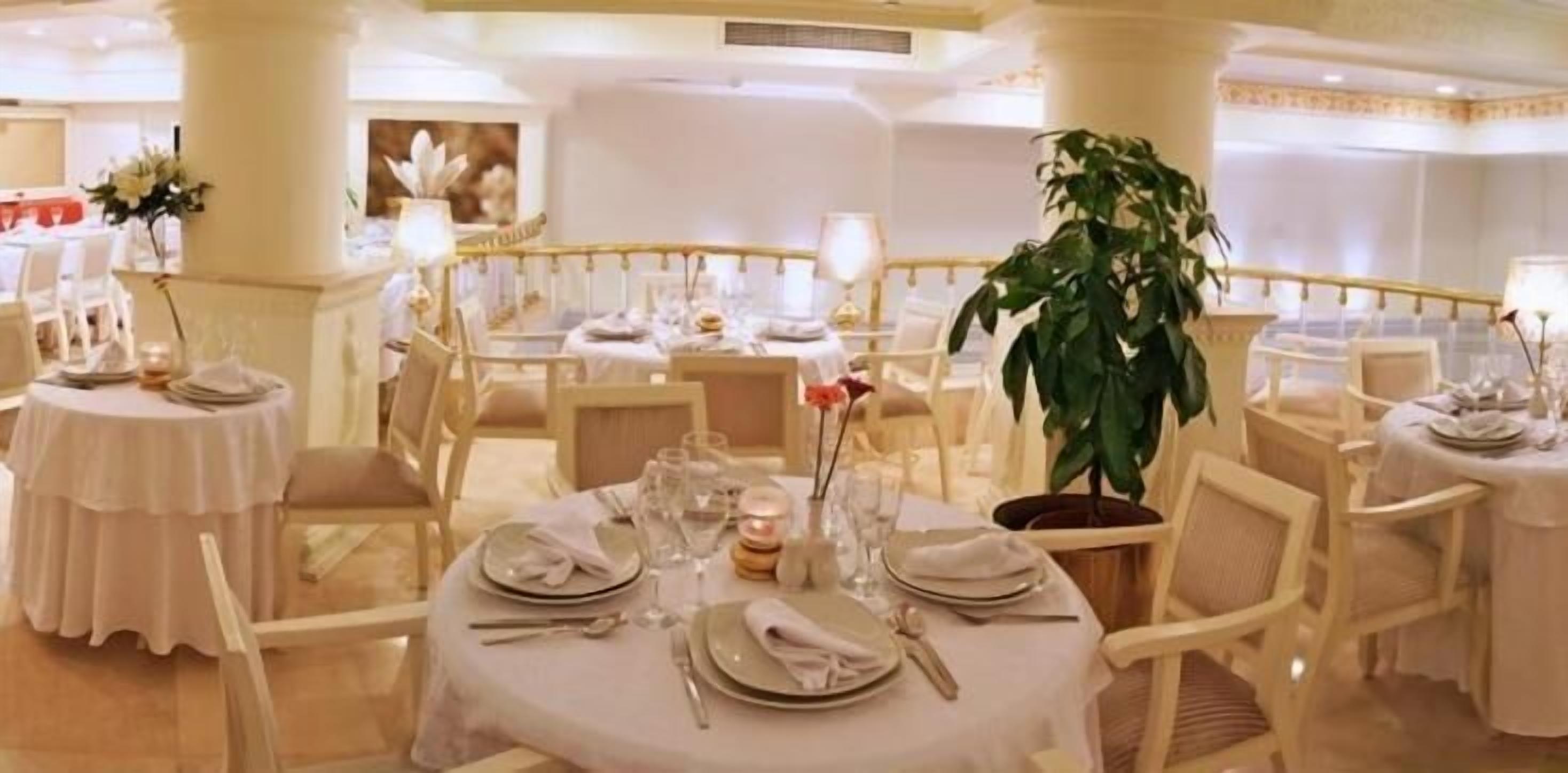 A formal dining area with round tables set for multiple guests, featuring white tablecloths, neatly arranged cutlery, and floral centerpieces.
