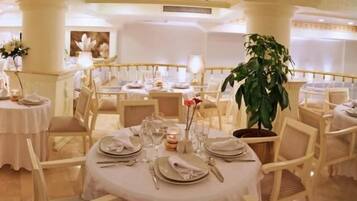 A formal dining area with round tables set for multiple guests, featuring white tablecloths, neatly arranged cutlery, and floral centerpieces.