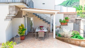 A covered patio with a dining table set for two, surrounded by potted plants and a staircase leading to an upper level. - Villa Totti (Sant'Agnello)