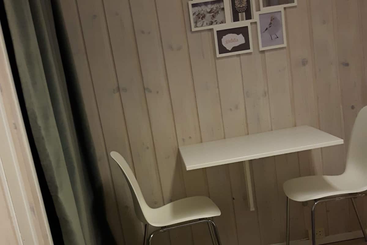 A room with a bed, two chairs, a small table, and a wall with framed pictures.