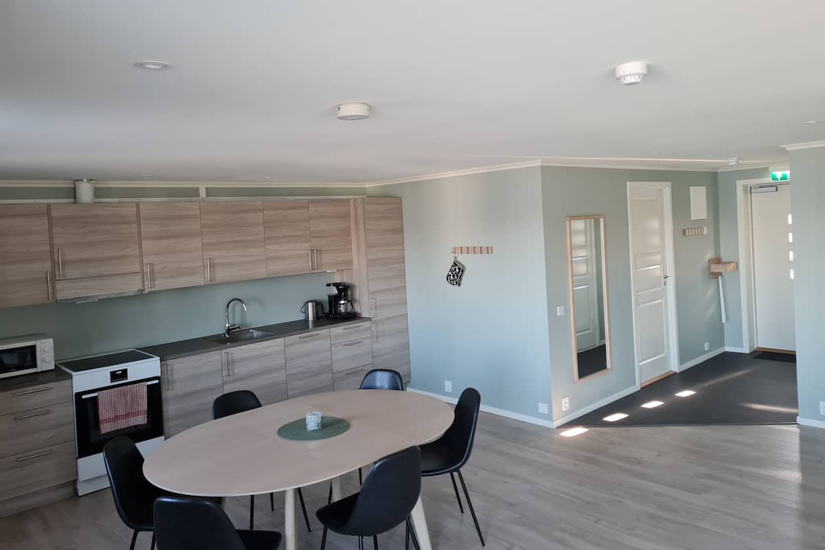 A modern kitchen with wooden cabinets, a dining table with chairs, and a small oven.