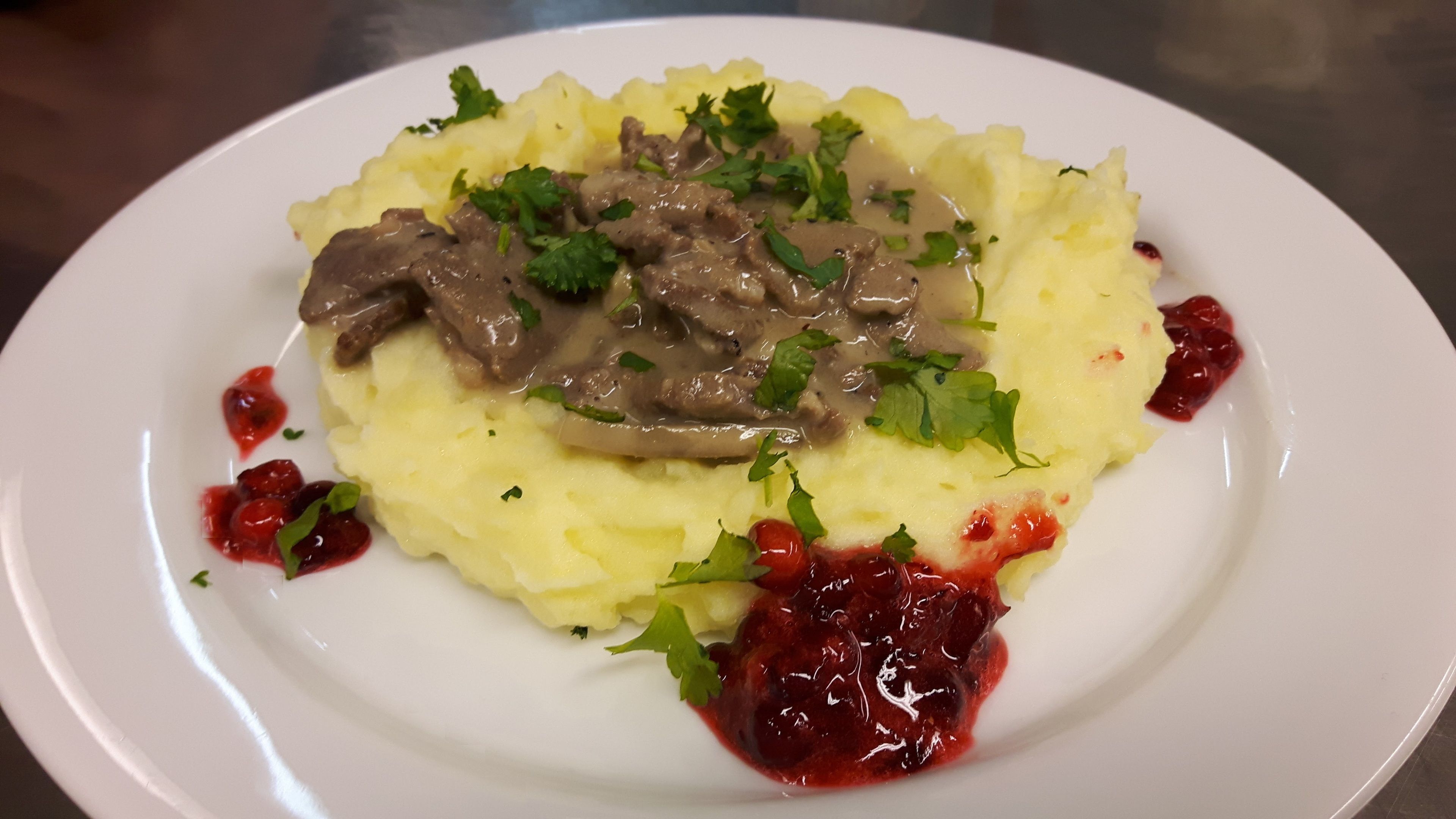 A plate of mashed potatoes topped with a mushroom sauce and garnished with parsley, served with a side of cranberry sauce.