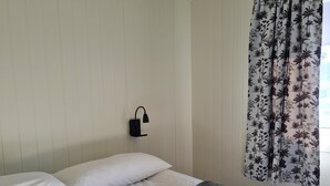 A hotel room with two beds, white bedding, a black wall-mounted lamp, and a window with floral curtains. - Olderfjord Turistsenter (Porsanger)