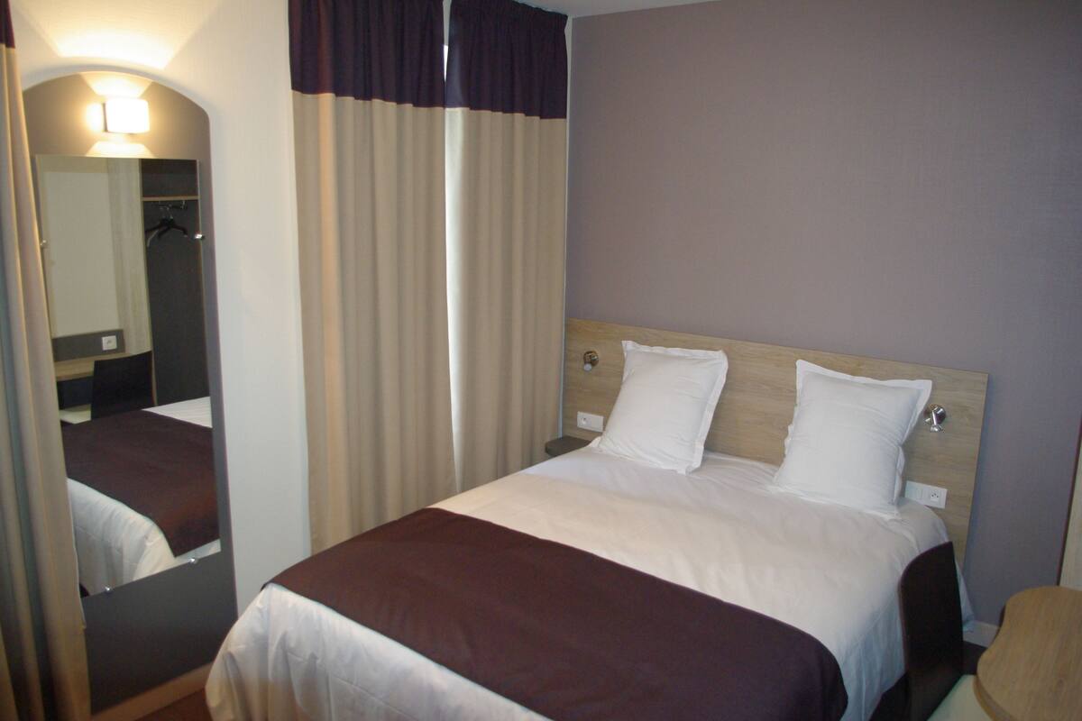 Ein Hotelzimmer mit Bett, Spiegel, Nachttisch und Stuhl.
