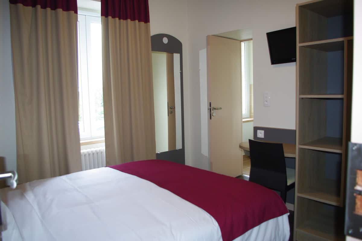 Ein Hotelzimmer mit Bett, Schreibtisch, Stuhl, Fernseher und Kleiderschrank.