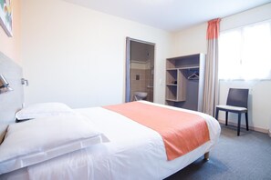 Une chambre d’hôtel avec un lit, une chaise, une armoire et une salle de bain visible à travers une porte ouverte.