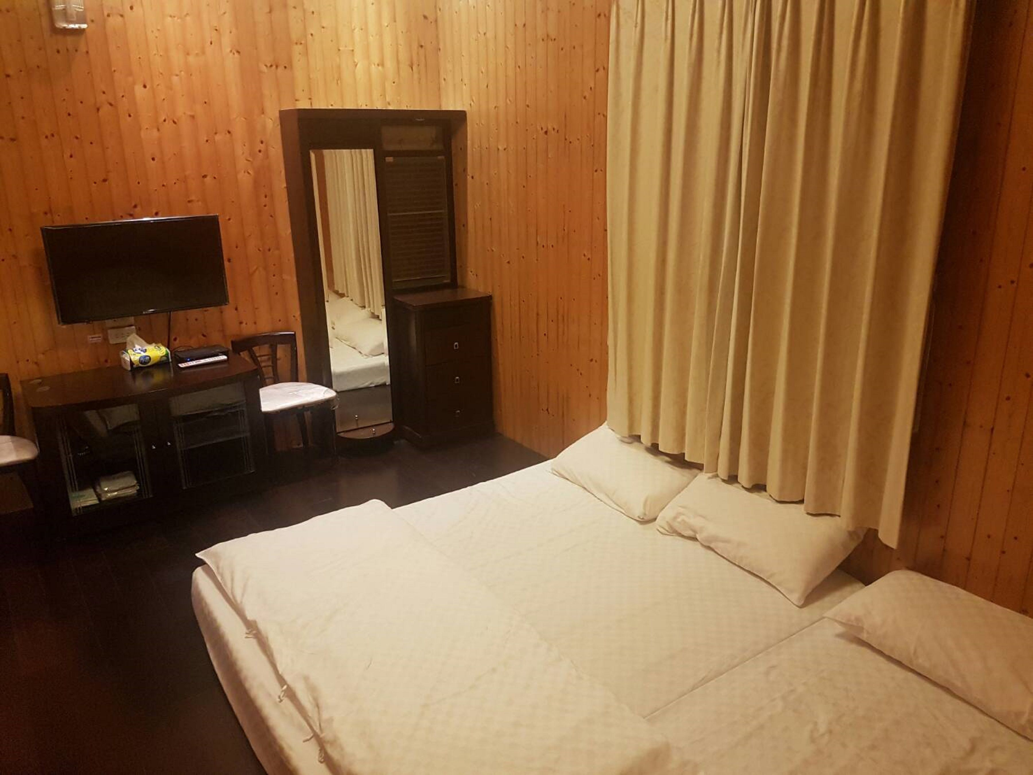 Een hotelkamer met een bed, een bureau met stoel, een televisie en een spiegel.