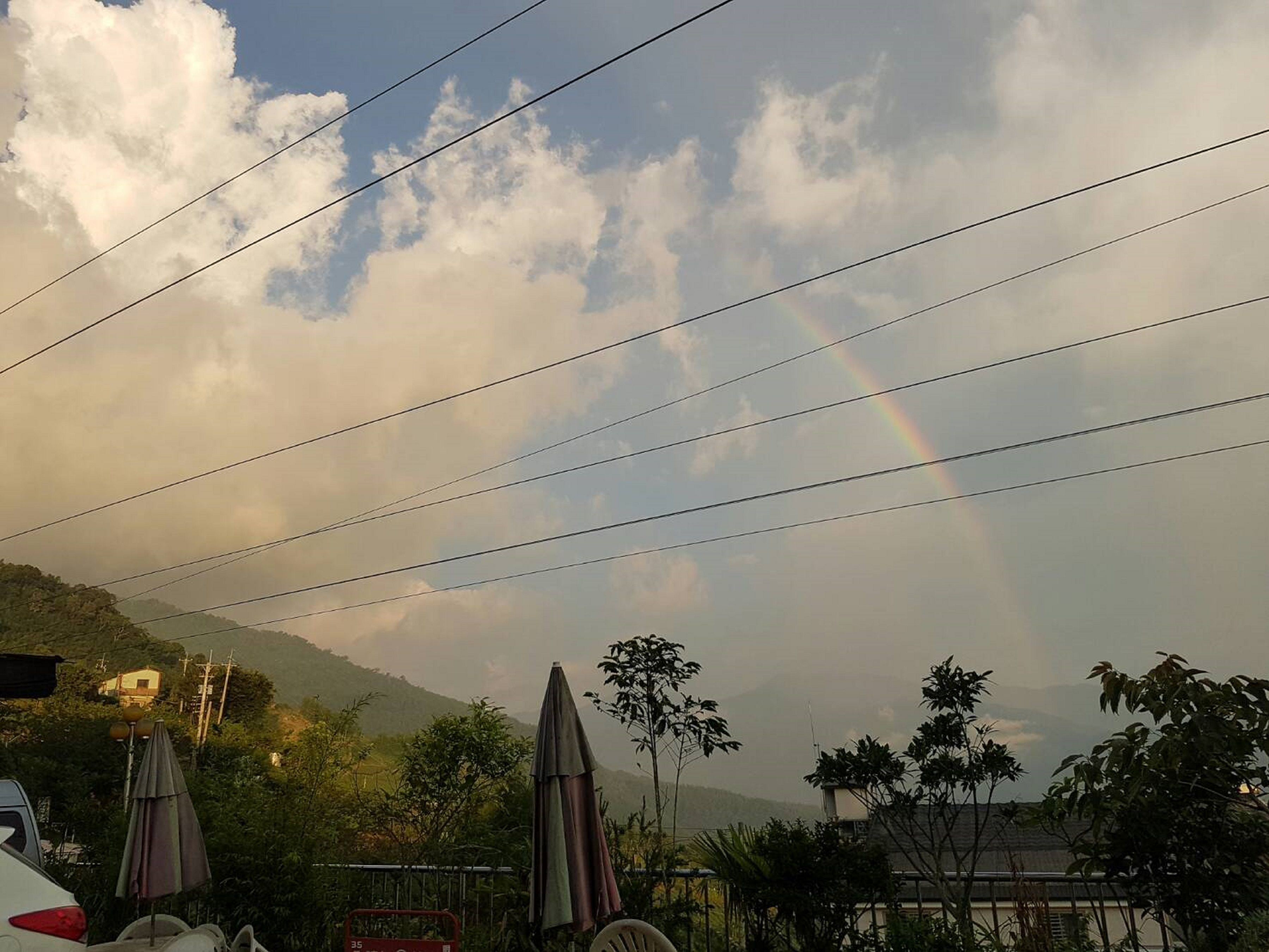 A view of a mountain with a rainbow, power lines, and a parked car.