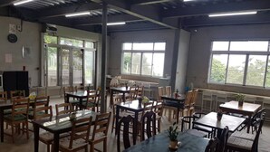 A spacious indoor dining area with multiple tables and chairs, large windows allowing natural light, and a visible clock on the wall. - Ming Yang B&B (Zhuqi)