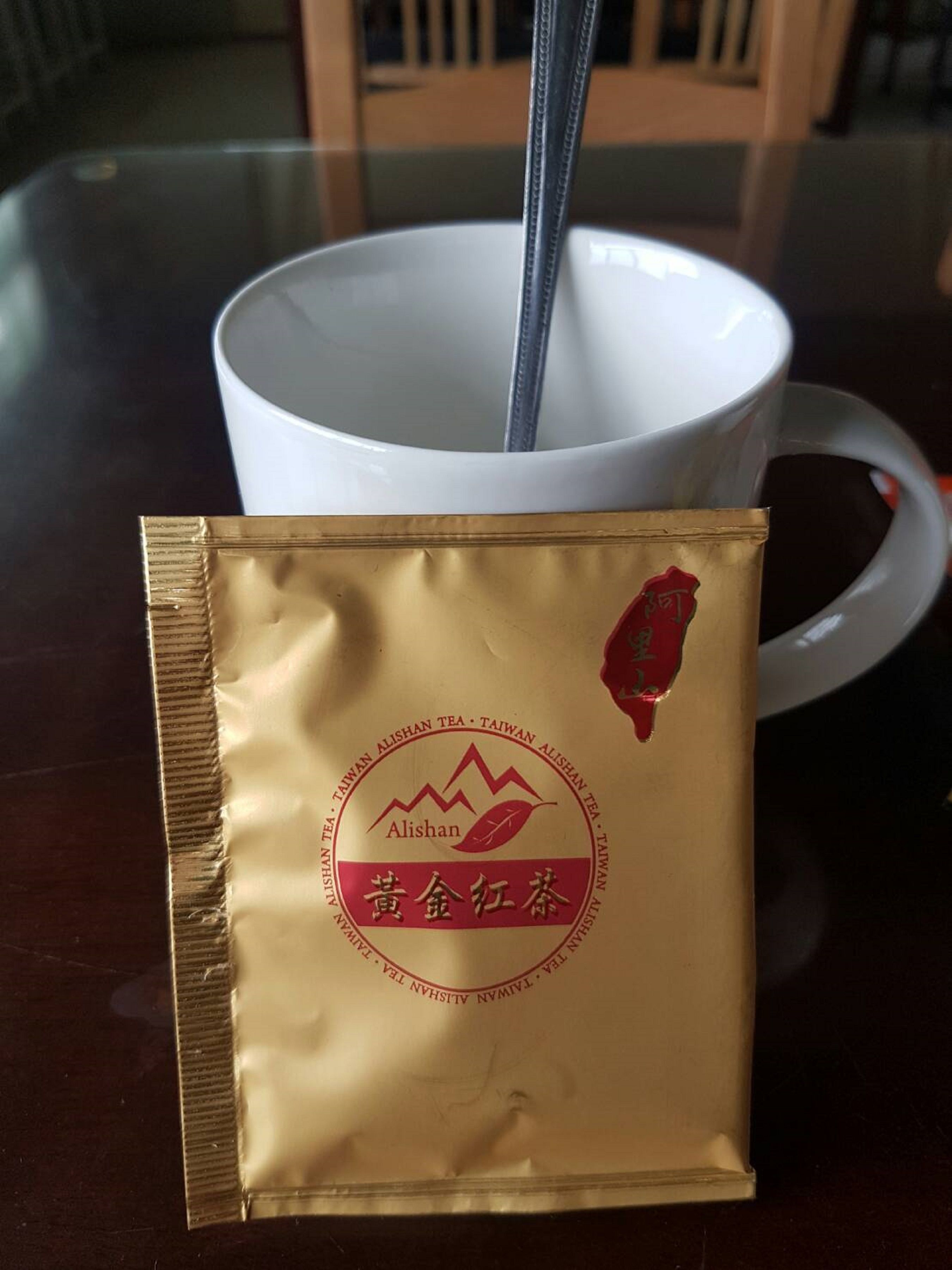 Un paquete de té Alishan con una cuchara en una taza blanca sobre una mesa.
