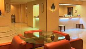 A lobby with a glass-top table surrounded by red leather sofas, a reception desk, and a large chandelier. - Hotel Ascent Hamamatsu (Hamamatsu)
