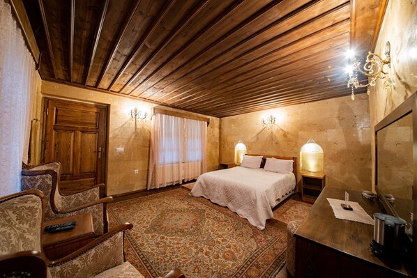 A room with a wooden ceiling, a bed with white linens, a nightstand with a lamp, a wooden chair, and a small table with a remote control.