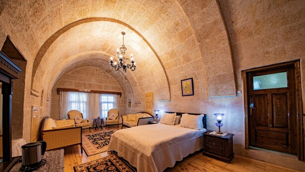 Une chambre avec un grand lit, un plancher en bois, un plafond en arc de cercle, un lustre et une porte en bois.