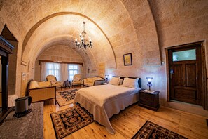 Une chambre avec un grand lit, un plancher en bois, un plafond en arc de cercle, un lustre et une porte en bois.