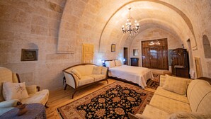 Une pièce dotée d’un haut plafond voûté en pierre, d’un lustre, d’un lit, de deux fauteuils, d’un plancher en bois et d’un tapis à motifs.