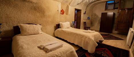 A room with two beds, a chandelier, and a rustic stone wall.