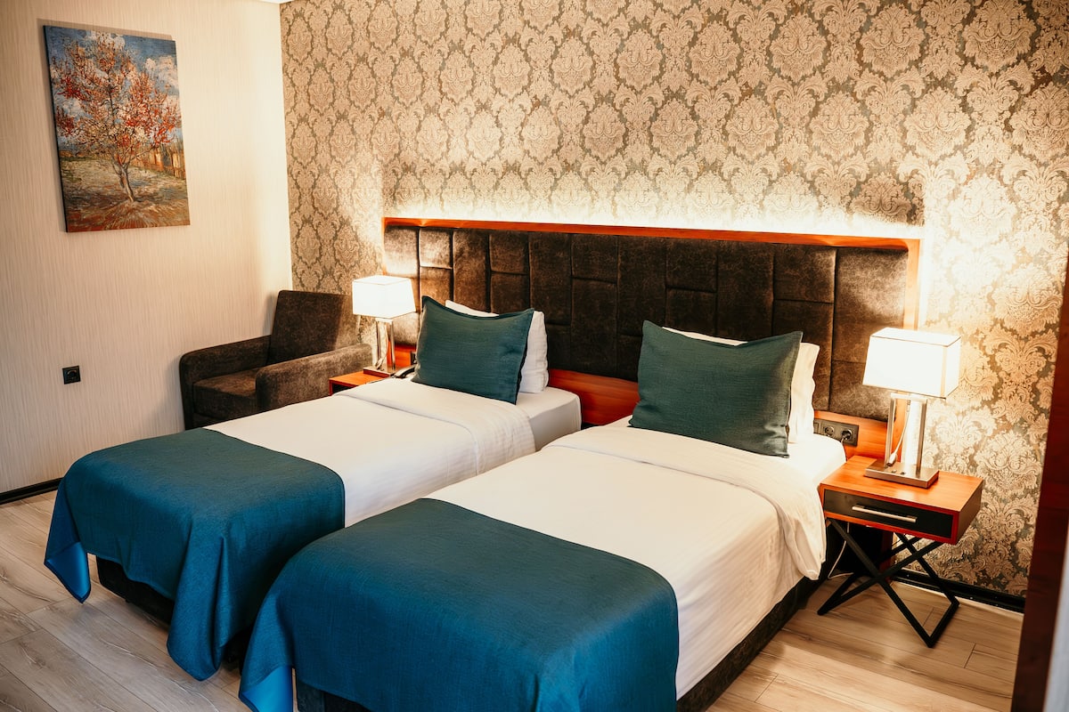 A hotel room with two beds, a nightstand, a chair, and a painting on the wall.