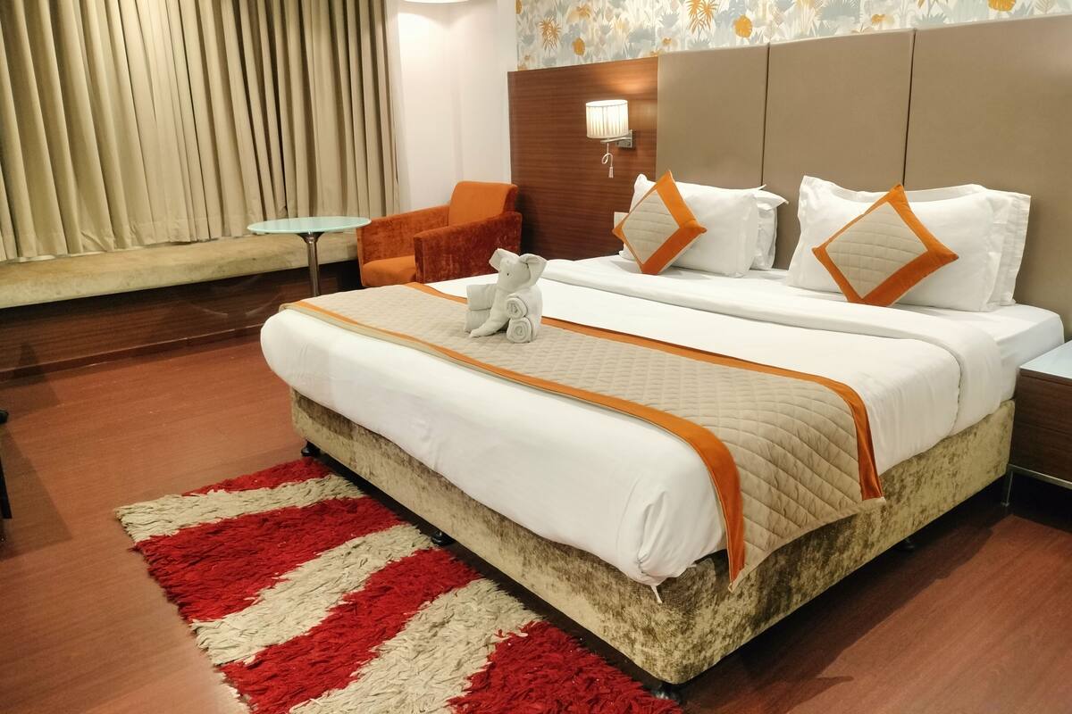 A hotel room with a large bed, two nightstands, a chair, a small table, and a window with curtains.