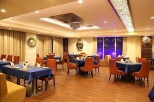 Comedor de hotel con varias mesas y sillas, un candelabro y decoración en las paredes.