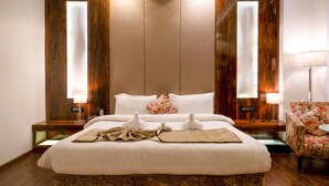 A large bed with white linens, two bedside lamps, and a floral-patterned armchair. - 5 Flowers Ananta Elite, Kota (Kota)