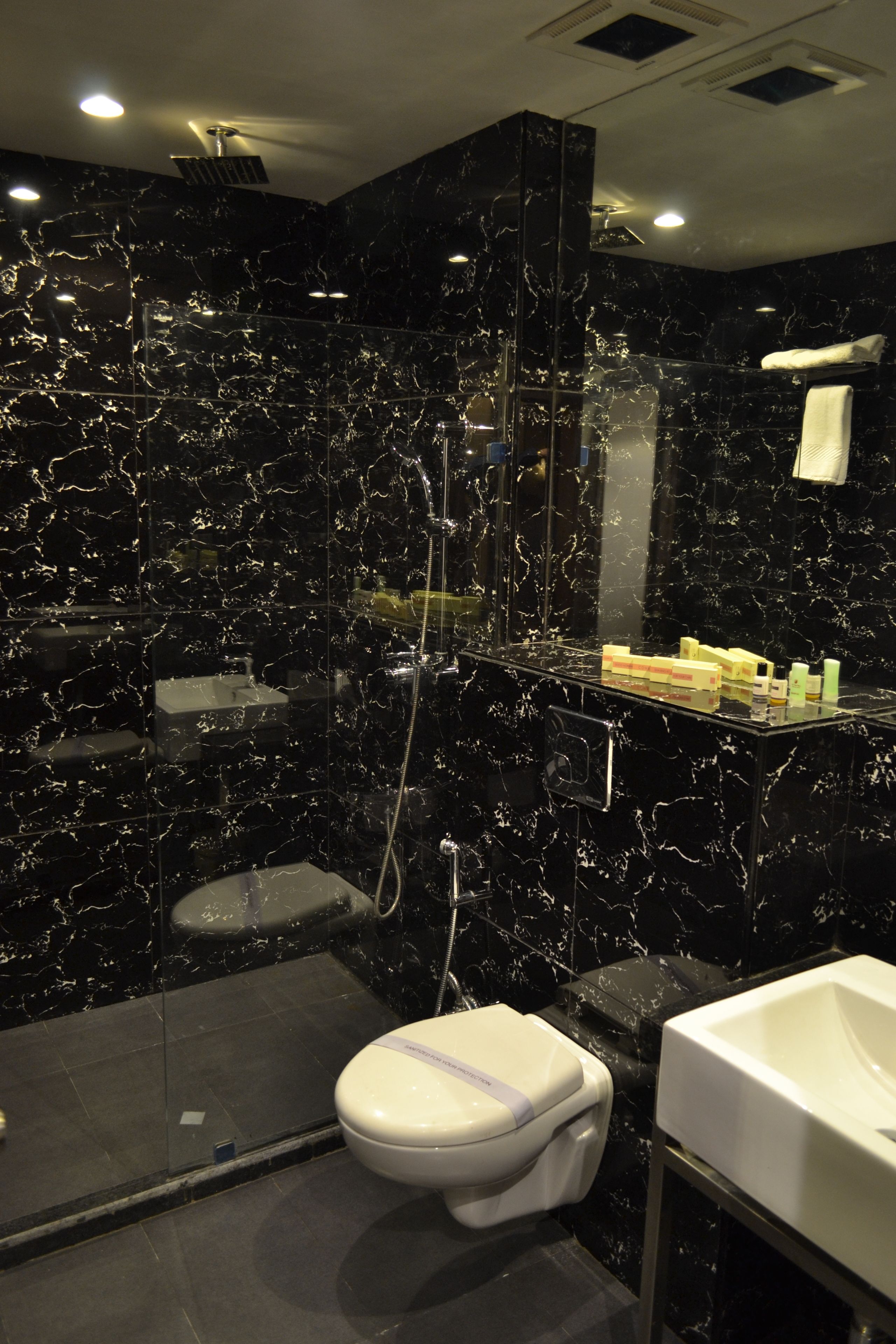 Un bany modern amb un disseny de marbre negre, un vàter blanc, un lavabo i una zona de dutxa.