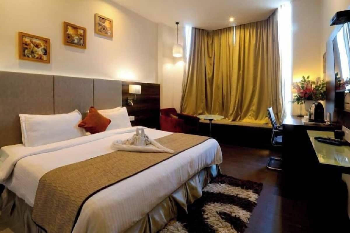 A hotel room with a large bed, a desk, a chair, a TV, and a window with curtains.