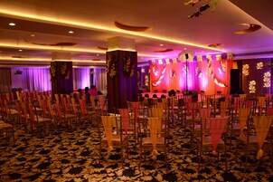 A banquet hall with rows of chairs, a stage with draped curtains, and floral decorations.