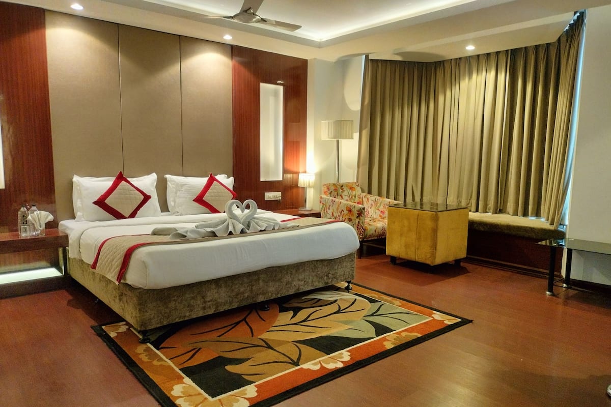 A hotel room with a large bed, a chair, a desk, and a window with curtains.