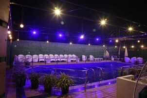 Una piscina exterior con sillas de descanso y sombrillas, rodeada de plantas en macetas.