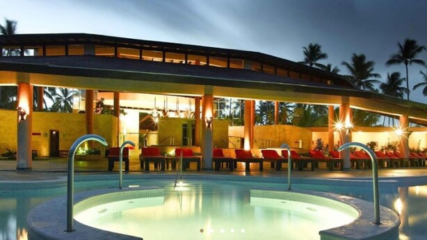 Ein Hotel mit Schwimmbad, Sitzgelegenheiten im Freien und Palmen im Hintergrund.