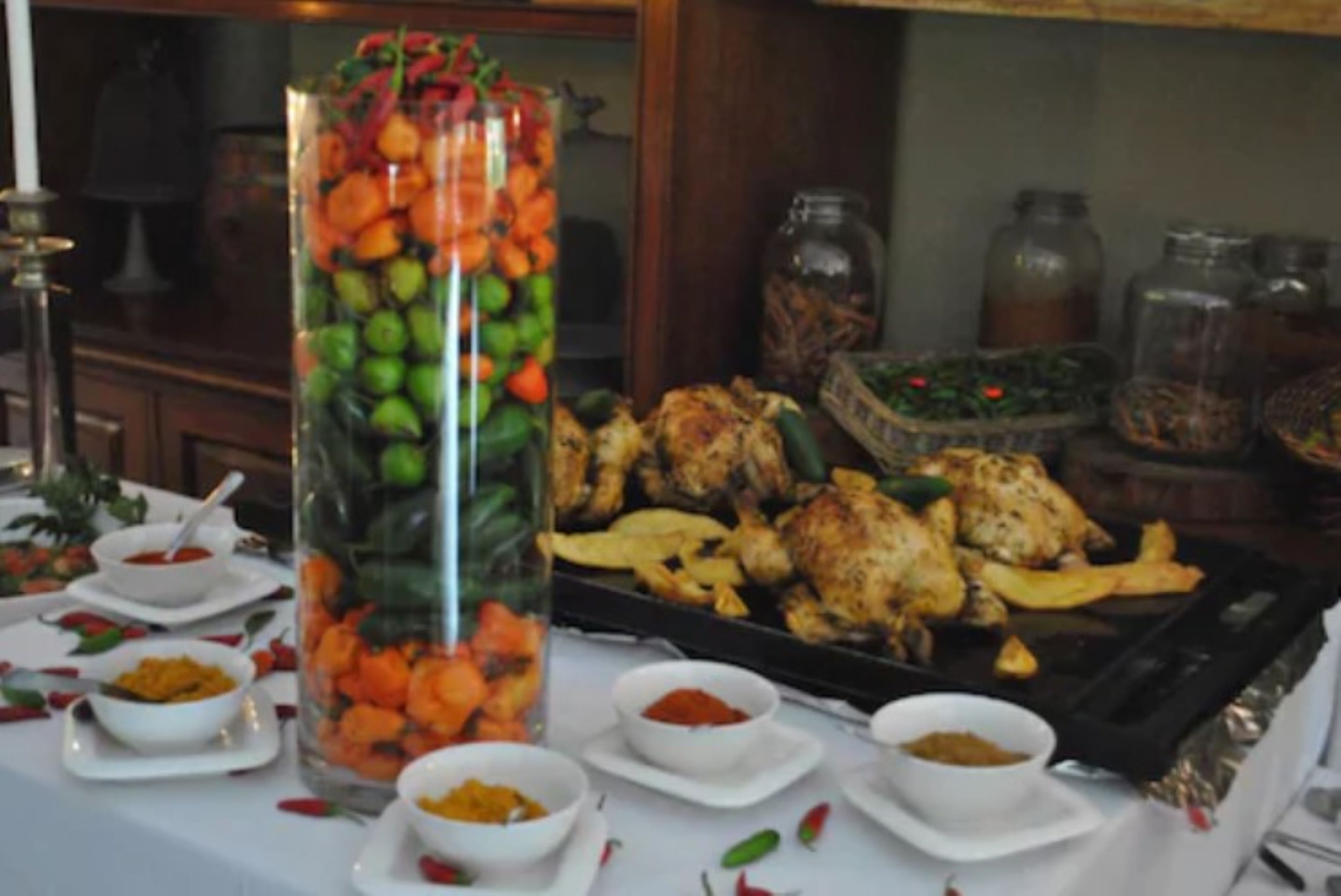 Une table de buffet proposant divers plats, notamment un grand récipient en verre rempli de fruits et de légumes, ainsi que plusieurs petits bols de sauces.