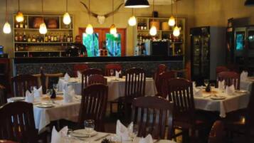 A restaurant with tables set for dining, a bar area with bottles, and a television screen.