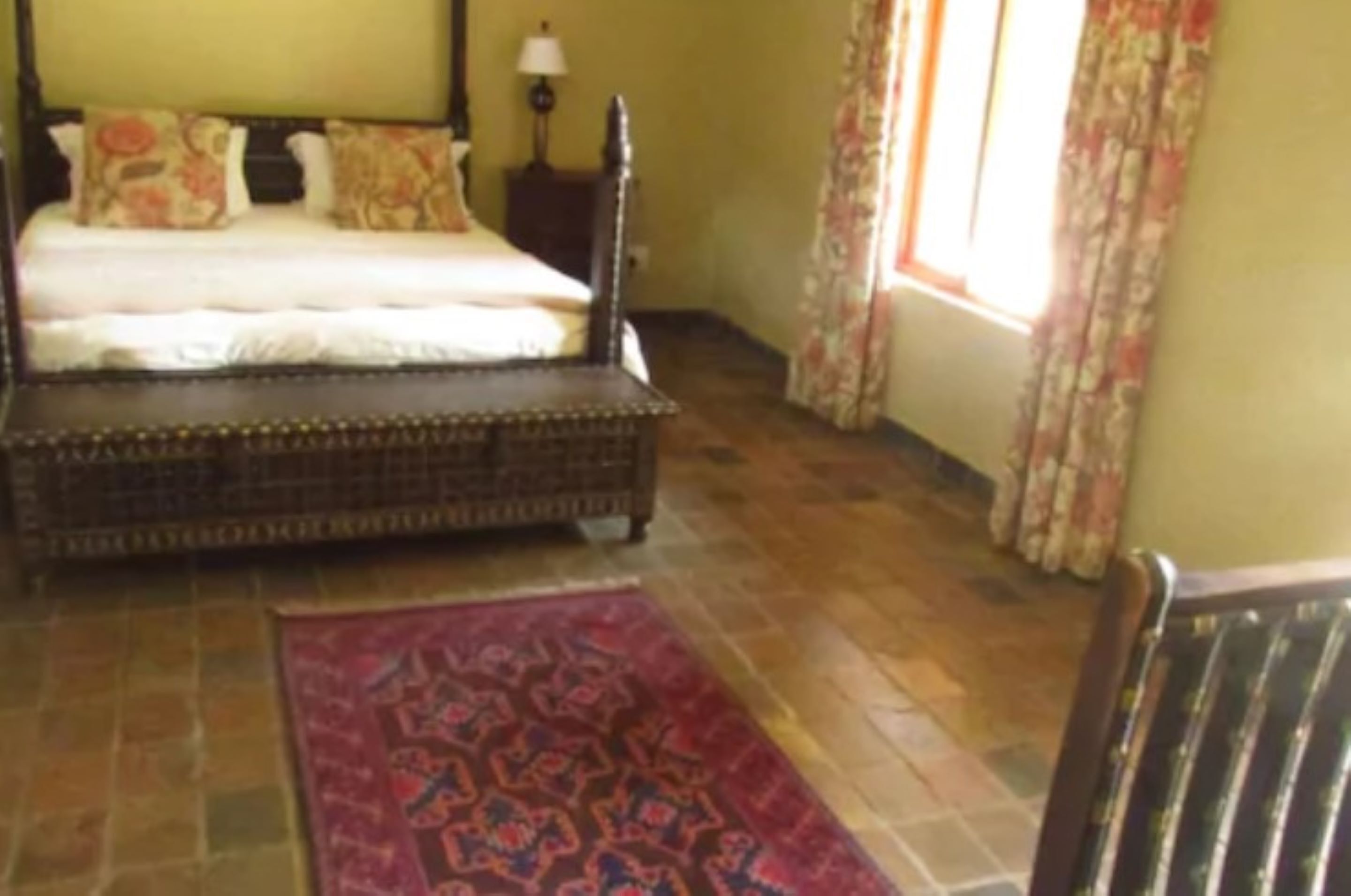 Un dormitorio con cama, mesita de noche, lámpara y ventana con cortinas.
