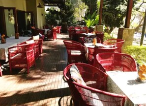 An outdoor seating area with red chairs and tables, surrounded by greenery and trees. - Willows Boutique Hotel (Pretoria)