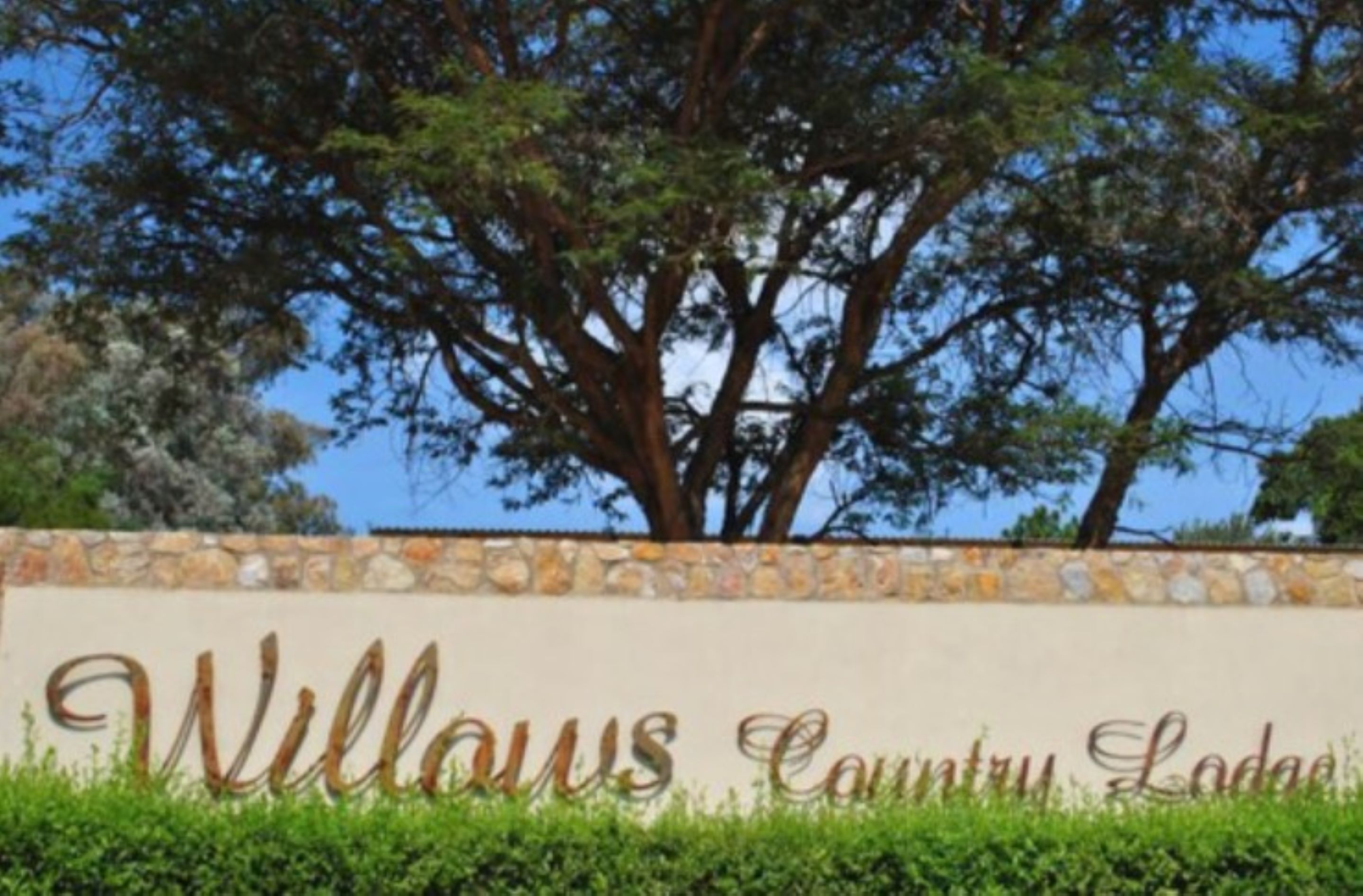 A sign for Willows Country Lodge with a stone wall and a large tree in the background.