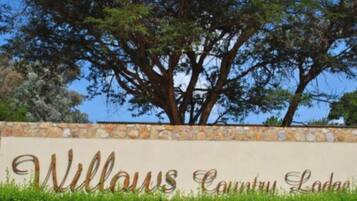 A sign for Willows Country Lodge with a stone wall and a large tree in the background.