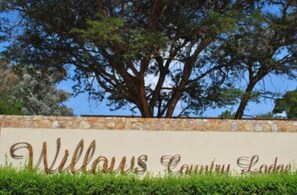 A sign for Willows Country Lodge with a stone wall and a large tree in the background. - Willows Boutique Hotel (Pretoria)