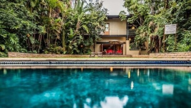 A pool with a house in the background surrounded by dense foliage.