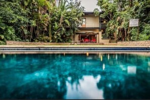 A pool with a house in the background surrounded by dense foliage. - Willows Boutique Hotel (Pretoria)