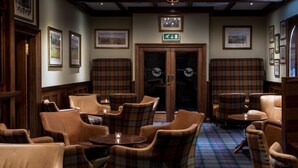 A lobby with plaid-patterned chairs and tables, framed pictures on the walls, and an exit sign above a door. - The South Beach Hotel (Troon)