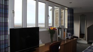 A hotel room with a large window, a television, a desk with a vase of flowers, and a mirror. - The South Beach Hotel (Troon)