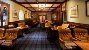 A hotel lobby with leather armchairs, a checkered carpet, wooden paneling, and framed pictures on the walls. - The South Beach Hotel (Troon)