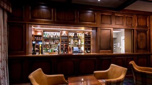 A bar area with wooden paneling, a well-stocked liquor shelf, and two upholstered chairs with a plaid tablecloth. - The South Beach Hotel (Troon)